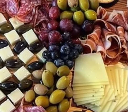Tablero de charcutería con embutidos, quesos y frutas frescas.