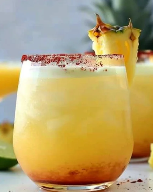 Margaritas de piña servidas en un vaso con decoraciones tropicales.
